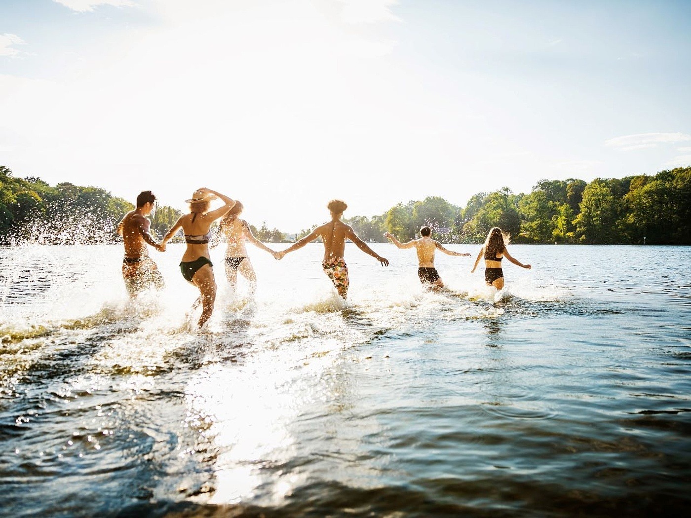 Mehrere Freunde rennen Hände haltend ins Wasser