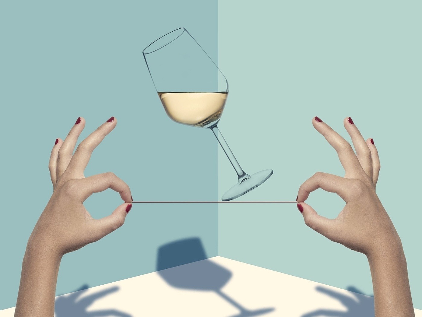 Ein scheinbar auf einem Faden schwebendes, gefülltes Weißweinglas umgeben von 2 Frauenhänden