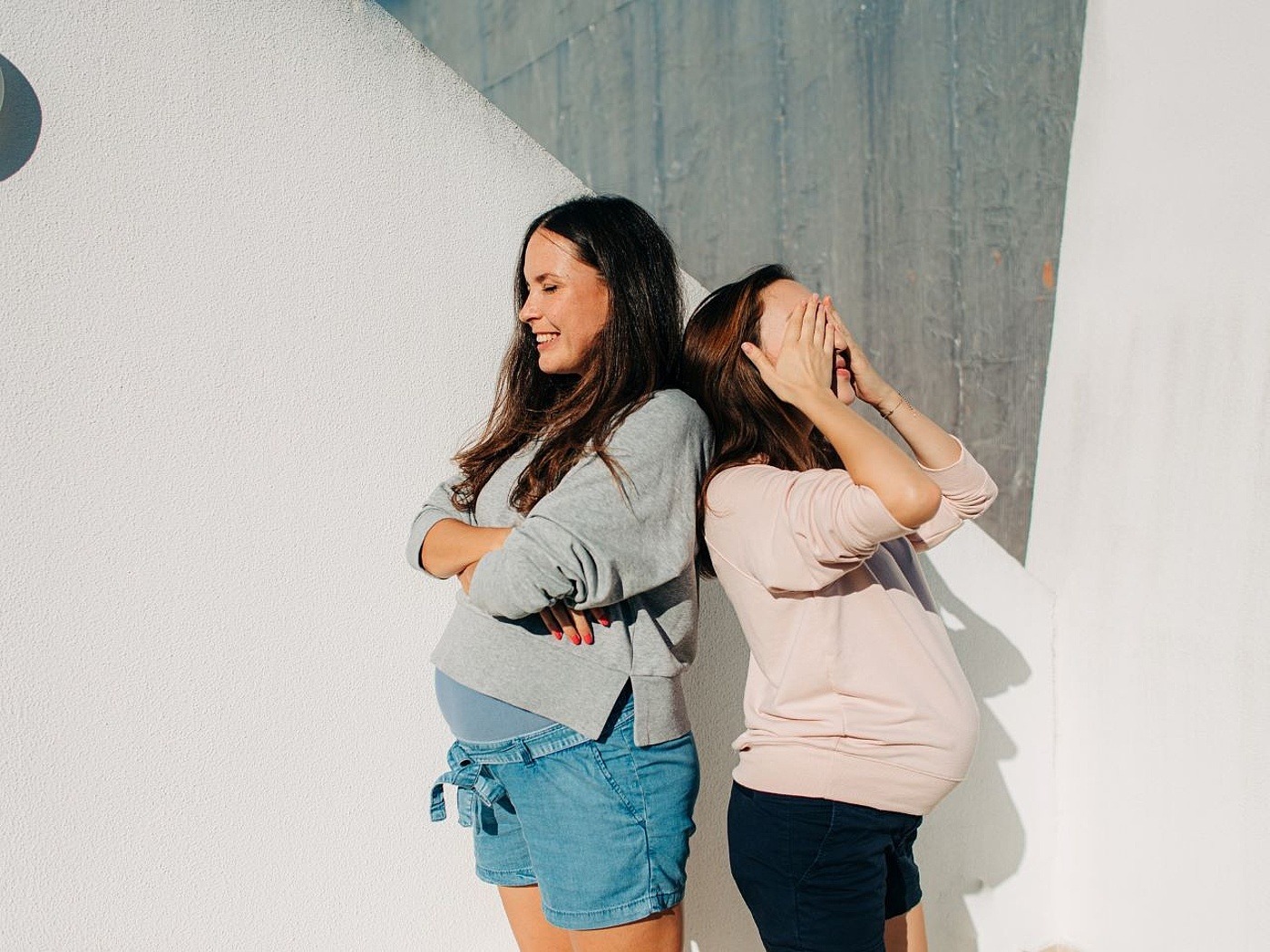 2 schwangere junge Frauen stehen Rücken an Rücken vor einer Wand