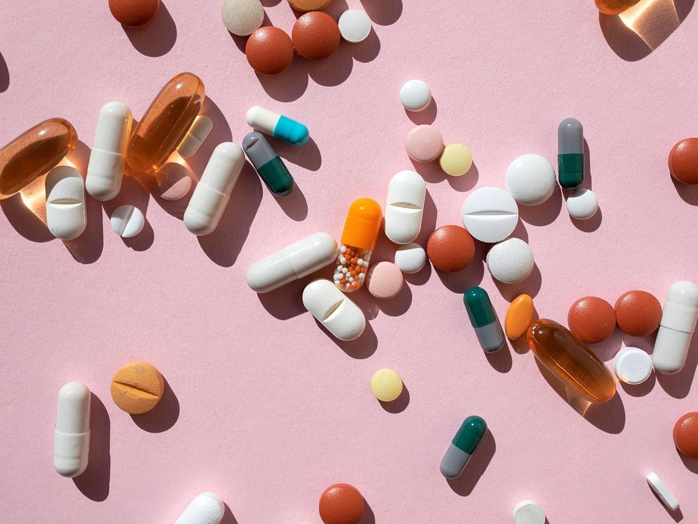 Verschiedene Tabletten verstreut vor hellrosa Hintergrund