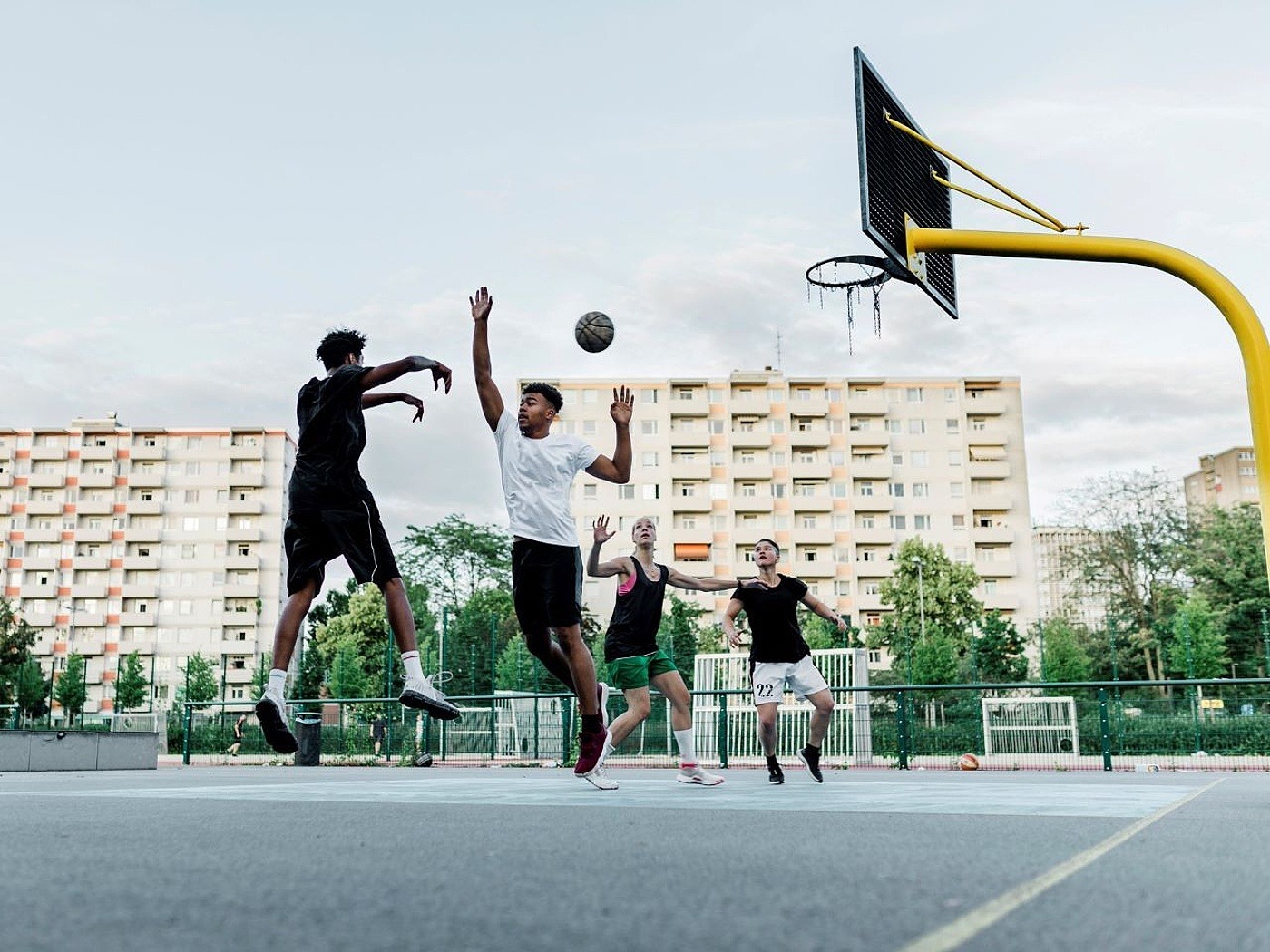 4 Jugendliche spielen Basketball auf einem Asphaltplatz