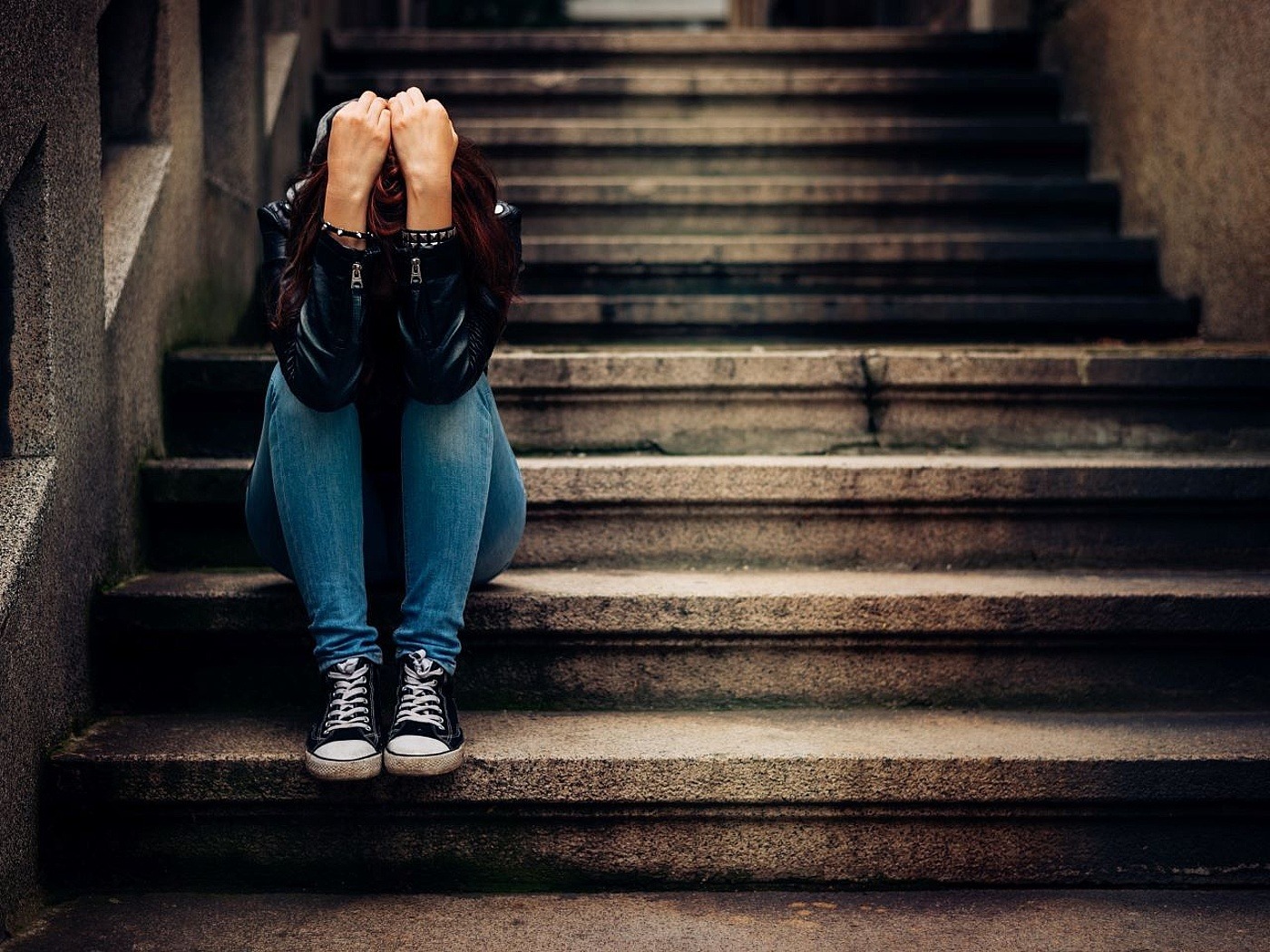 Junge Frau sitzt mit dem Kopf in ihren Händen traurig auf einer Treppe